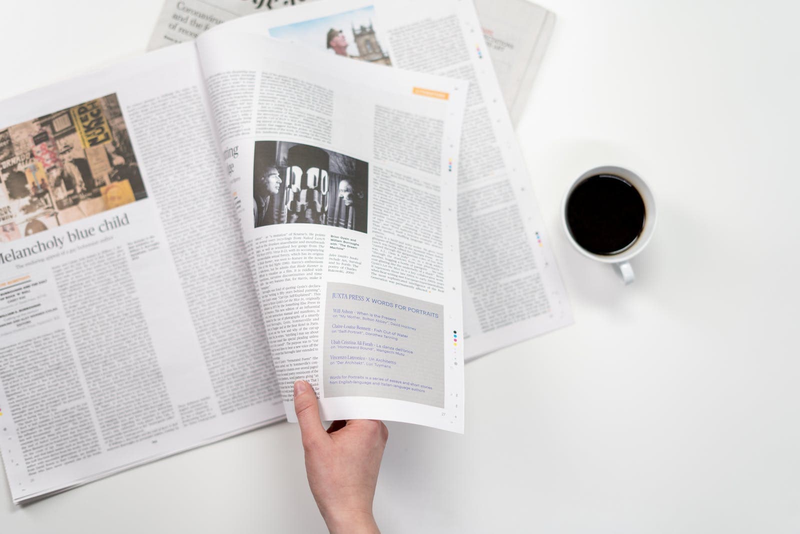Iemand die een papieren krant vasthoudt en een kopje koffie naast zich heeft staan
