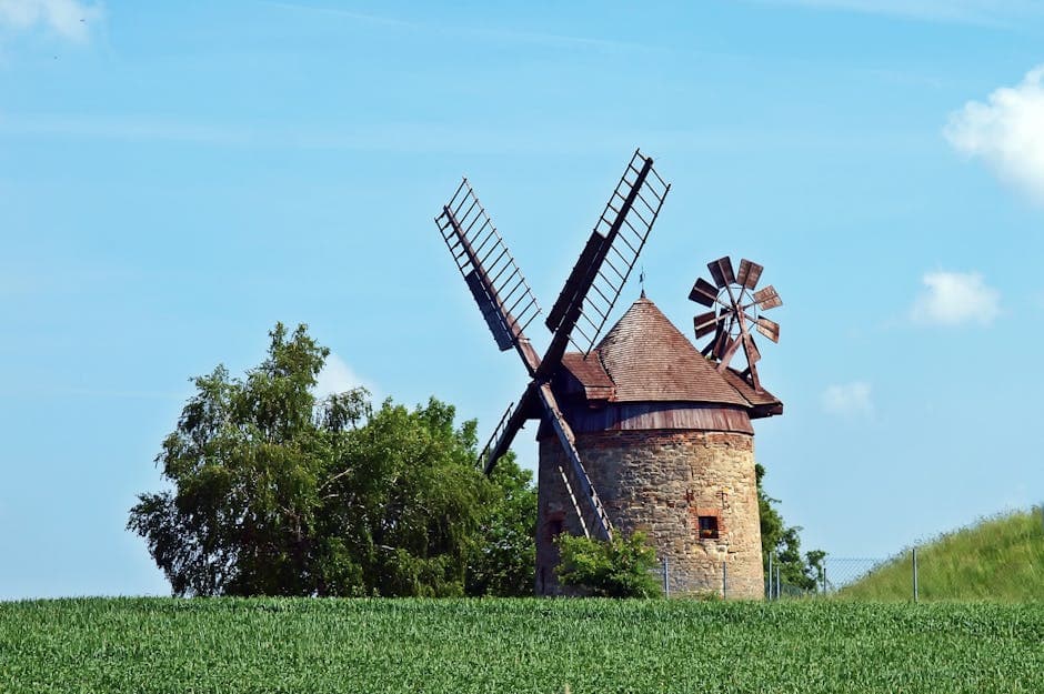 Bruingrijze windmolen naast een groene boom onder een blauwe bewolkte lucht tijdens de dag.