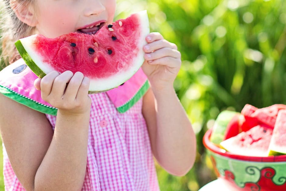 Meisje dat watermeloenfruit naast tafel eet